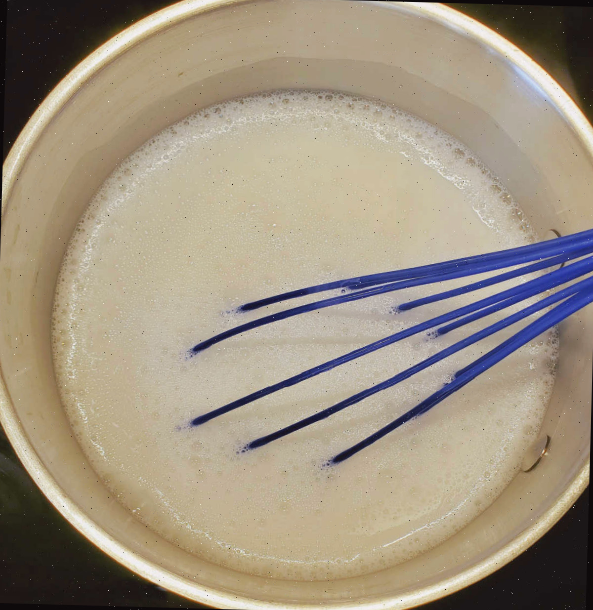 Fazendo sabão líquido. Uma panela no fogão preparando sabão líquido. O batedor azul está apoiado dentro do líquido.