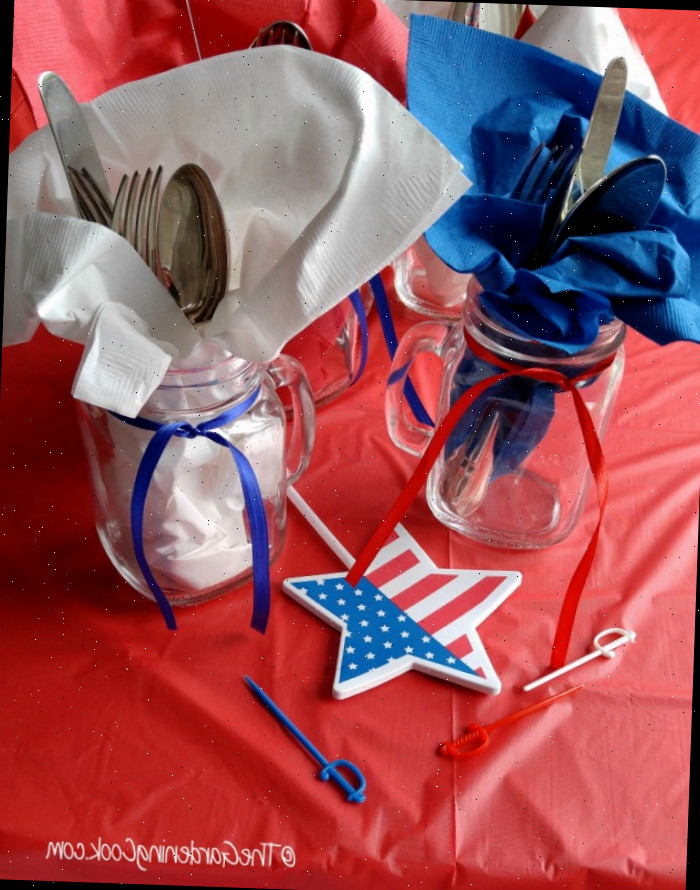 Suportes de Talheres Patriotic Mason Jar com toalhas azuis e brancas, fitas vermelhas e azuis e estrelas de bandeira em uma toalha de mesa vermelha.
