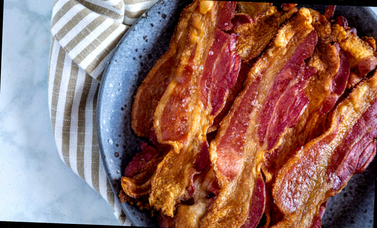 Bacon no forno sem bagunça em uma tigela azul ao lado de uma toalha listrada.