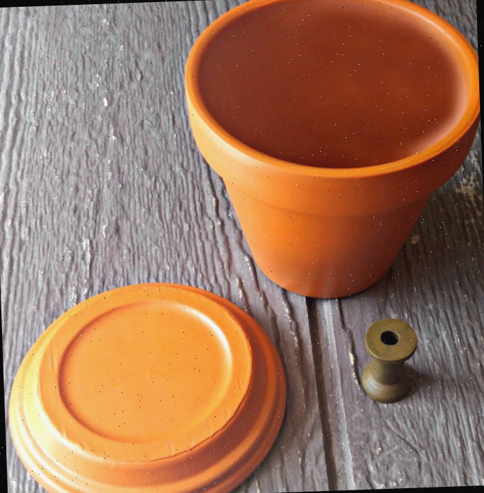 vasos de barro pintados Vaso de barro e prato pintados de laranja e um carrete de madeira pintado de verde amarelado.