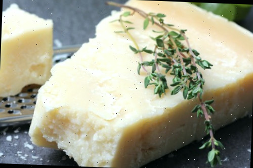 Um bloco de queijo parmesão coberto com tomilho ao lado de um ralador de queijo.