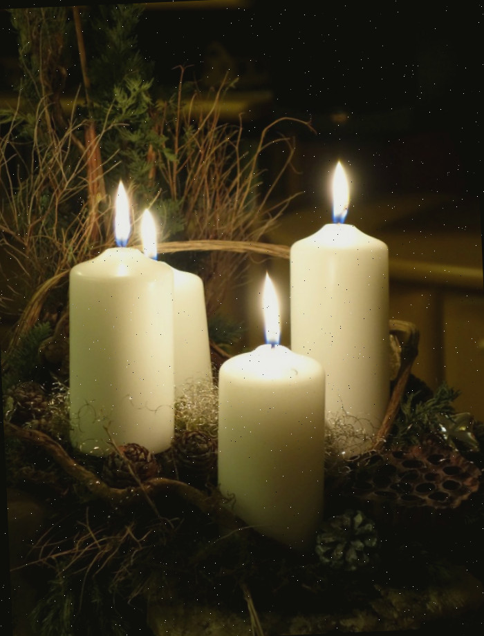 Velas brancas acesas em uma cesta com folhagens secas.