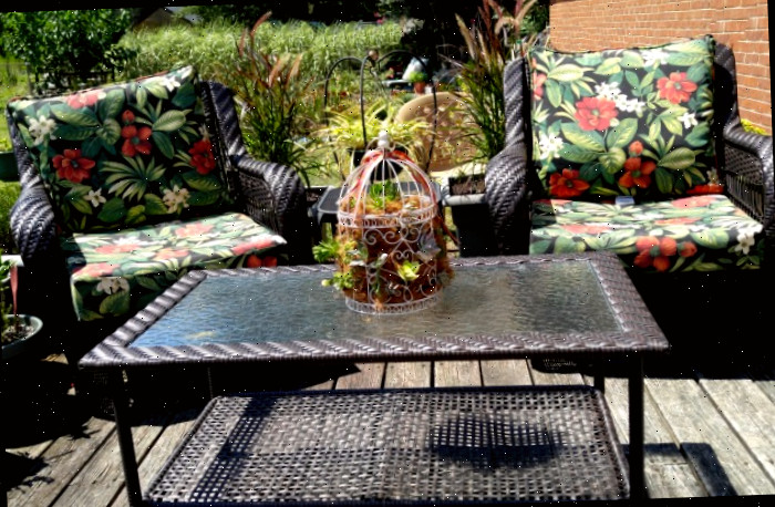 Duas cadeiras de pátio com almofadas coloridas próximas a uma mesa de pátio de rattan, que possui uma jardineira de gaiola de suculentas sobre ela.