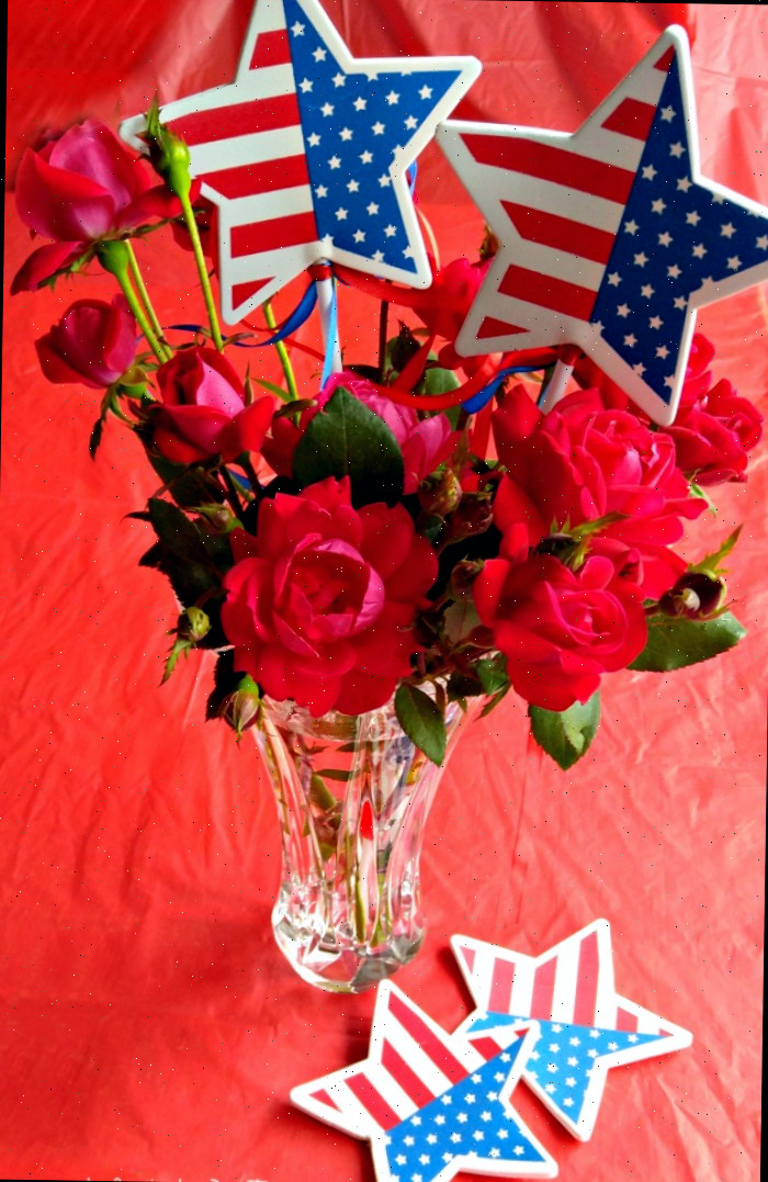 Decoração de vaso de rosas patrióticas com bandeiras estrela em uma toalha de mesa vermelha.
