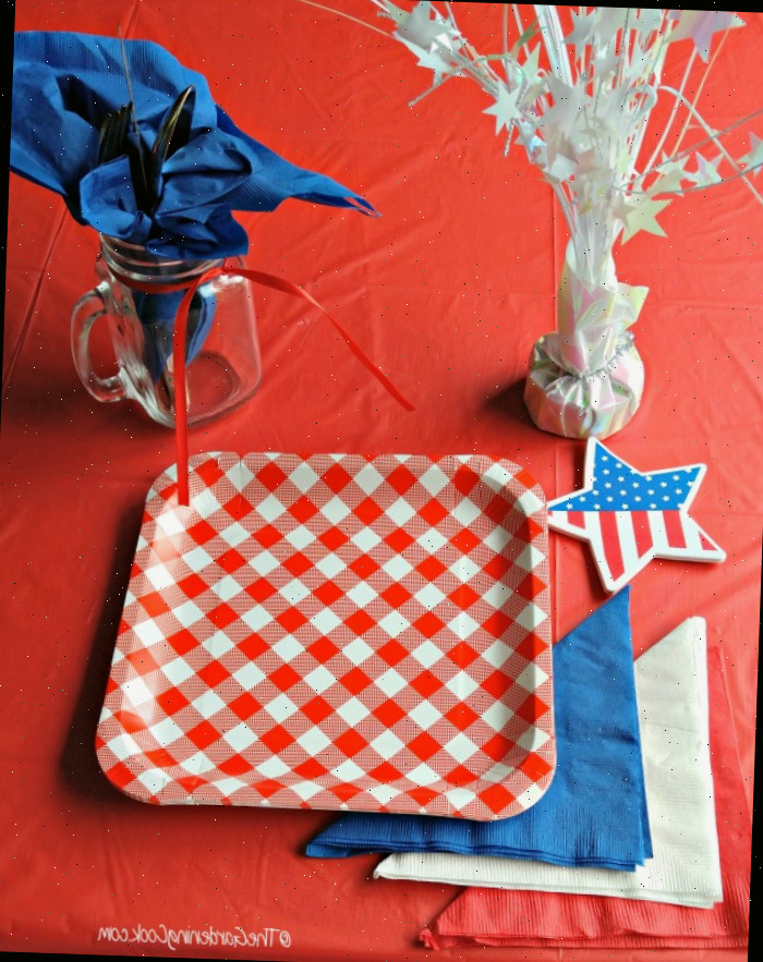 Montagem de mesa patriótica com peso de papel estrela, toalha azul em frasco de conservas, toalhas vermelhas, brancas e azuis, estrela de bandeira e pratos vermelhos e brancos.