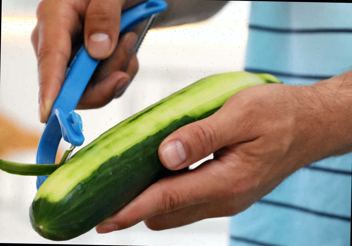 descascar um pepino Homem em uma camisa azul descascando um pepino.