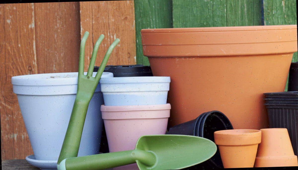 Um grupo de vasos de barro e vasos plásticos limpos com ferramentas de jardinagem, guardados em um galpão.