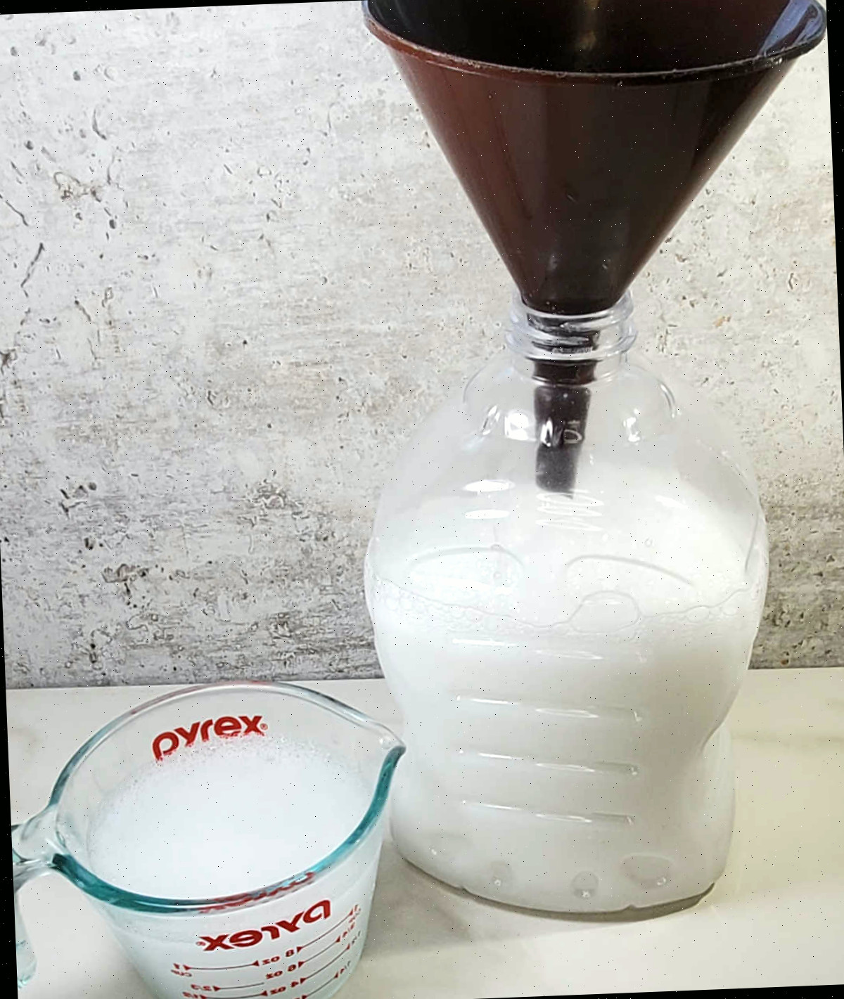 Transfira o detergente líquido para um frasco. Despejando detergente líquido caseiro em um grande frasco com um funil e um copo medidor com bico.