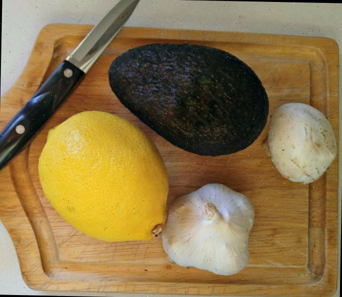 Abacate, limão, alho e cogumelo em uma tábua de cortar com uma faca.