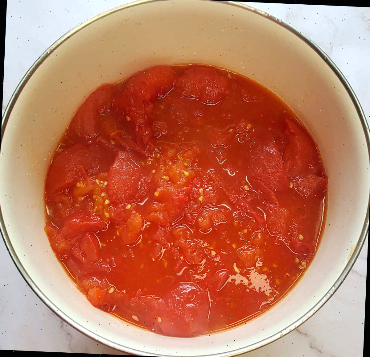 Tomates assados triturados para molho em uma tigela branca em uma bancada de mármore.