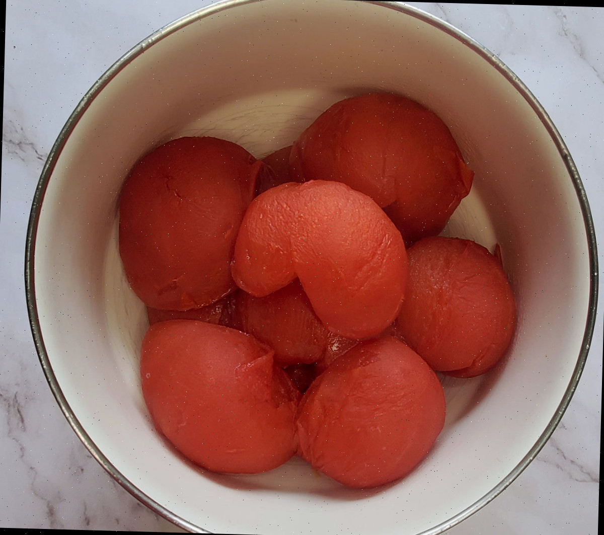 Metades de tomates beefsteak assados em uma tigela de cerâmica branca sobre uma bancada de mármore.