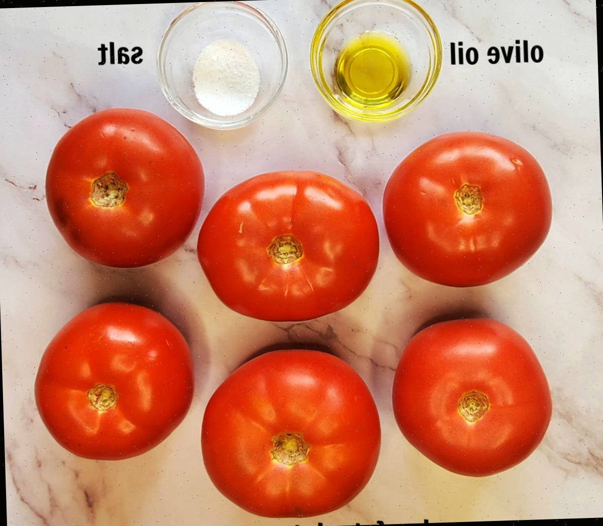6 tomates beefsteak e duas tigelas com azeite e sal, rotuladas com texto preto, em um balcão de mármore - ingredientes para torrar tomates para molho.