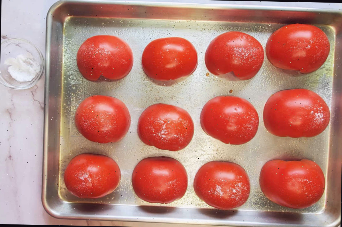 Tomates beefsteak cortados ao meio, temperados com sal em uma grande assadeira.
