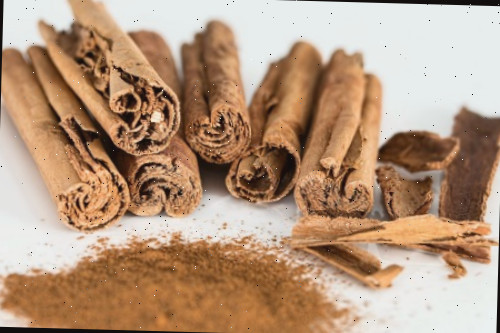 Canela em pau ao lado de um pouco de canela em pó.
