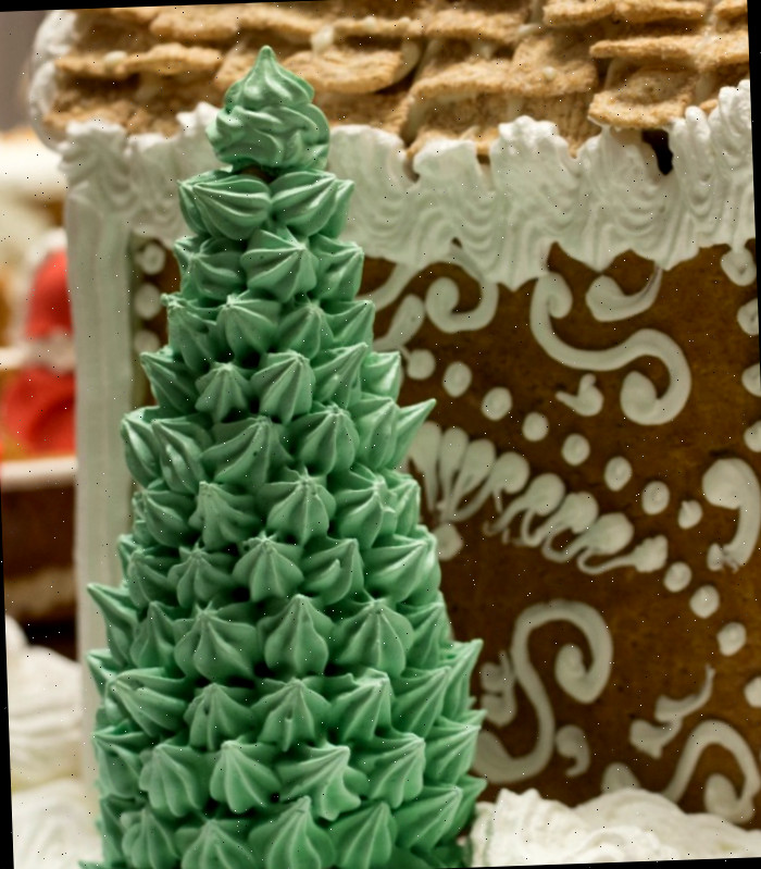 Uma árvore de Natal feita de cone de sorvete coberta com estrelas de cobertura verde perto de uma casa de gengibre decorada.