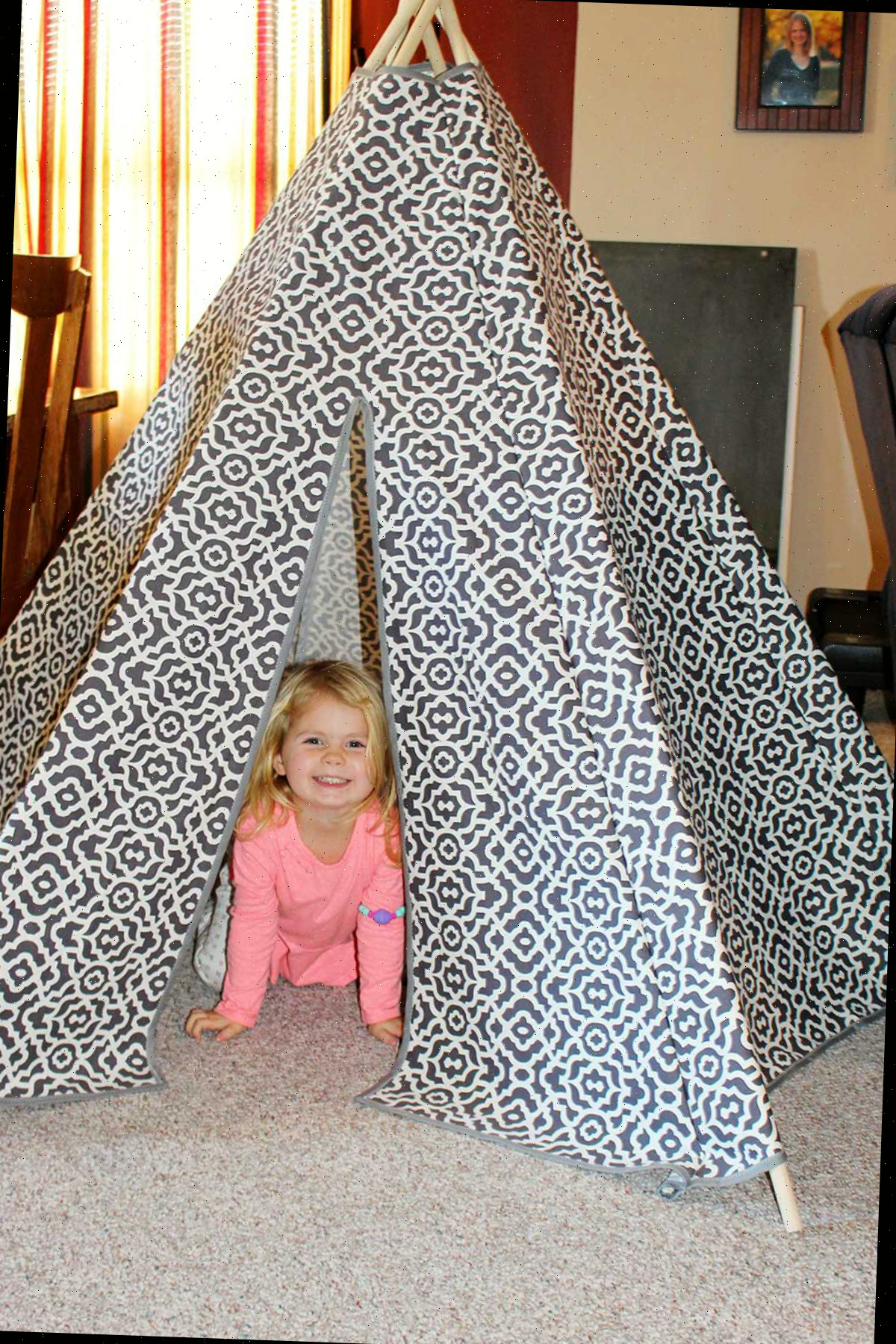 Uma criança pequena dentro de um toldo teepee DIY de tecido com padrões cinza e branco.