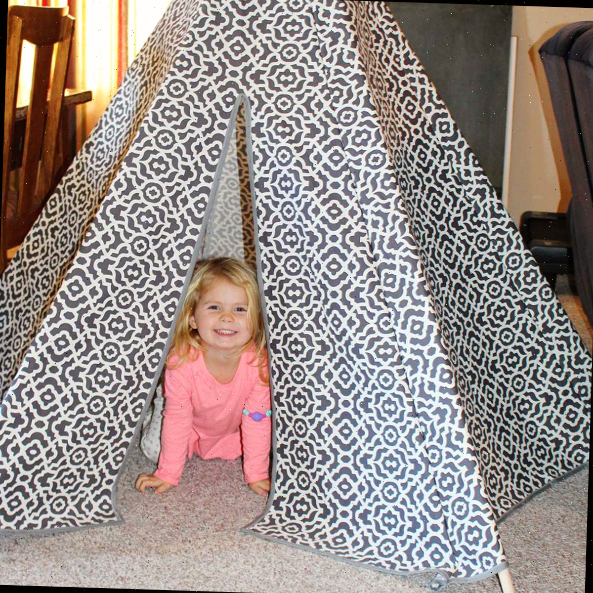 Uma criança pequena dentro de uma tenda teepee DIY feita de tecido estampado cinza e branco.