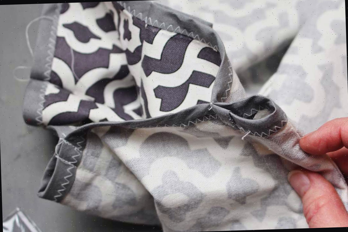Tecido cinza e branco decorado com bordas finalizadas com fita viés cinza, costurado em um laço para suportar varas de madeira para montar uma tenda teepee DIY.