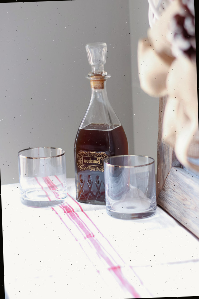 Decantador vintage de bourbon com copos de highball com borda dourada sobre um caminho de mesa de saco de grão vermelho e branco