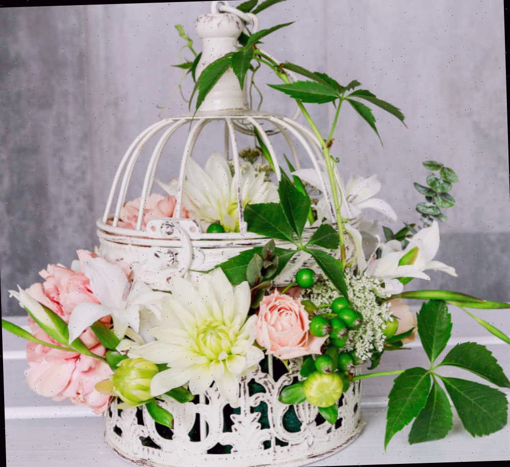 Arranjo de flores em uma gaiola de pássaro. Linda gaiola de pássaro branca com flores e folhas de seda.