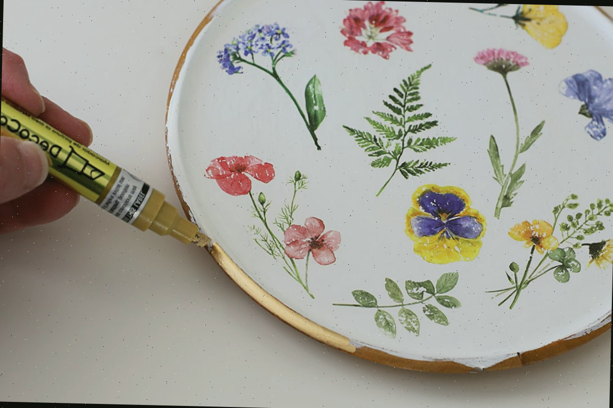 Usando um marcador de tinta para aplicar folha de ouro ao perímetro de um prato de madeira.
