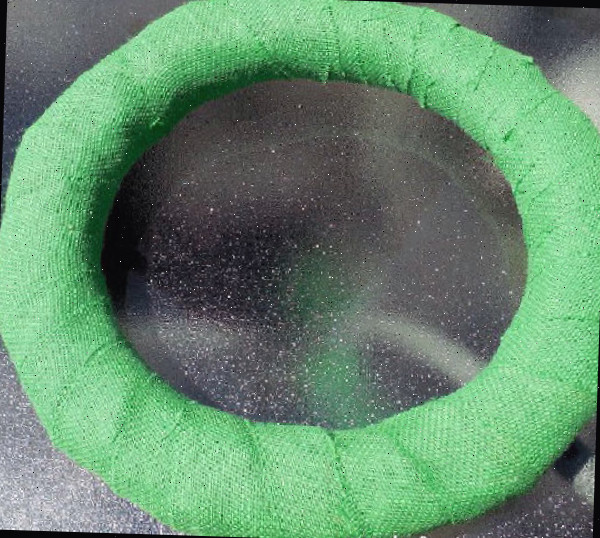 Uma forma redonda de guirlanda coberta com juta verde em uma mesa de vidro.
