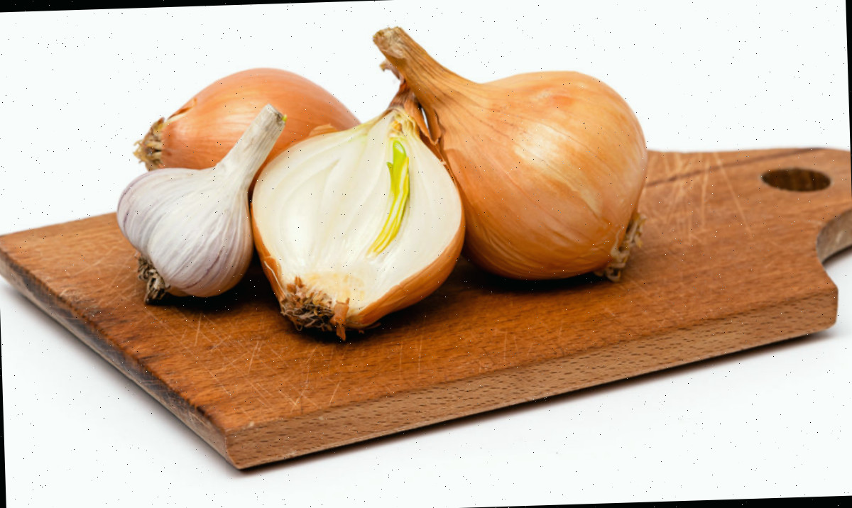 Cebolas amarelas e alho em uma tábua de corte de madeira para serem usados no lugar das chalotas em uma receita.